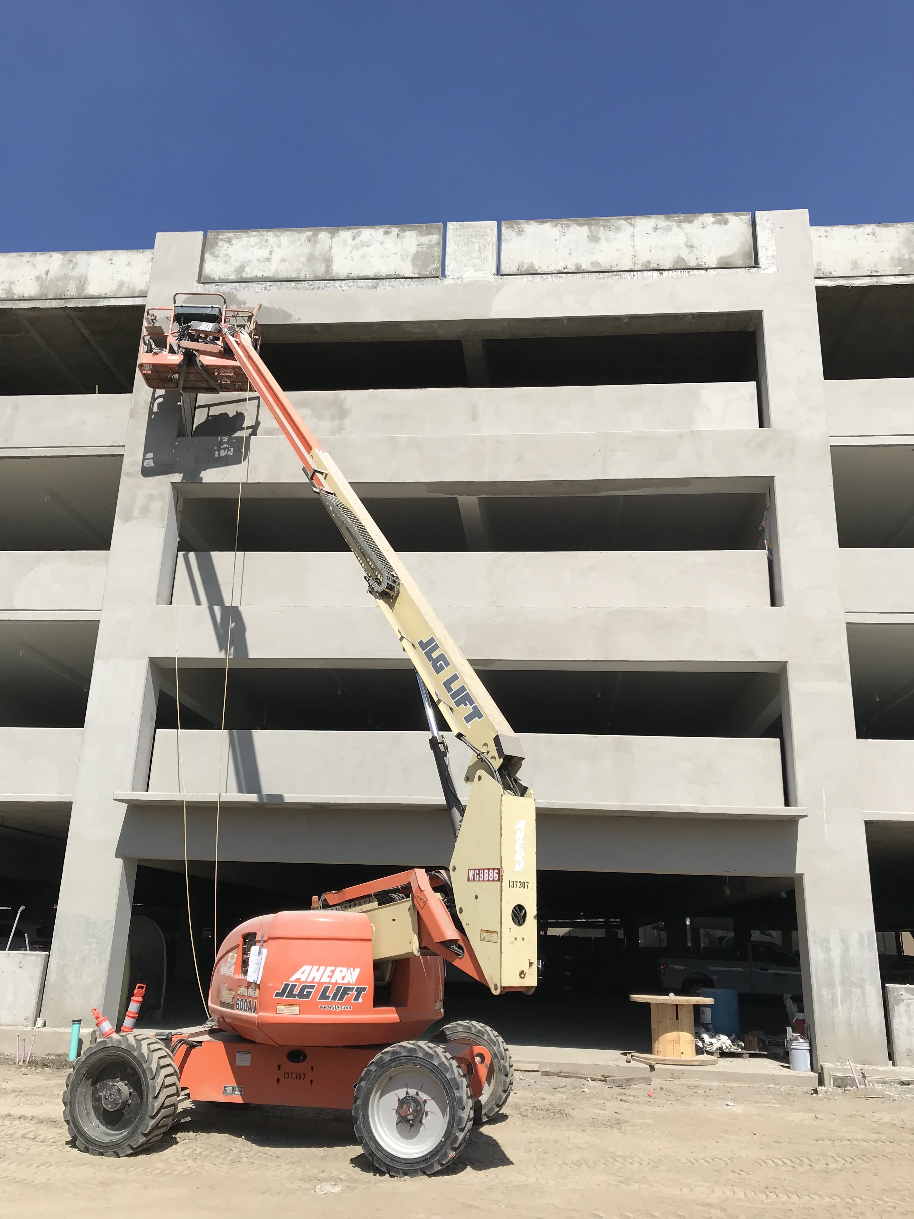 Boom lift in front of a concrete and steel parking structure